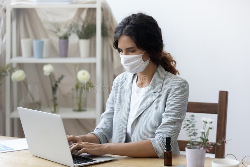 Woman employee in medical mask work on laptop in office