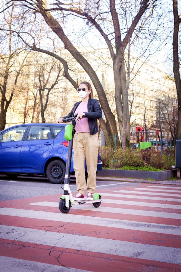 Young woman wearing face mask while using electric scooter during the coronavirus pandemic in the city. Full length shot of young woman wearing face mask while stock images Young woman wearing face mask while using electric scooter during the coronavirus pandemic in the city. Full length shot of young woman wearing face mask while stock images
