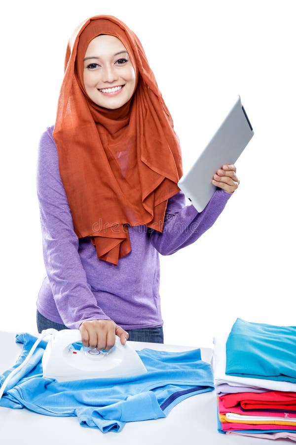 Young woman wearing hijab reading article on tablet while ironin royalty free stock image Young woman wearing hijab reading article on tablet while ironin royalty free stock image