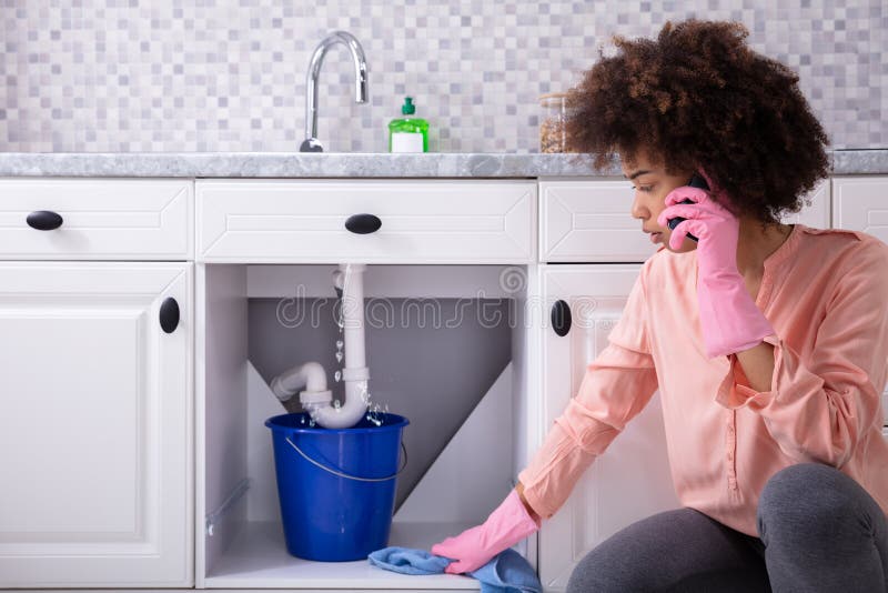Woman Calling Plumber In Front Of Leaking From Sink Pipe royalty free stock photography Woman Calling Plumber In Front Of Leaking From Sink Pipe royalty free stock photography