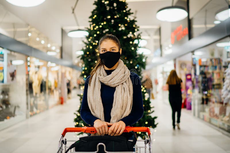 Young woman wearing protective face mask shopping in a mall, buying holiday presents.Holiday shopping.Christmas decoration in mall
