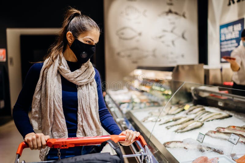 Young woman wearing protective face mask shopping in a supermarket,buying groceries.Seafood and fish shopping.Eating healthy food