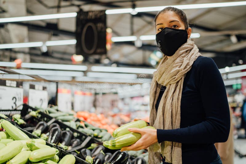 Young woman wearing protective face mask shopping in a supermarket,buying organic produce.Eating healthy food during coronavirus