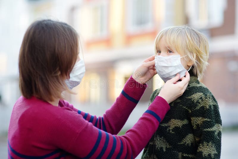 Young woman wearing a protective mask puts a face mask on a his son in airport, supermarket or other public place. Safety during stock images Young woman wearing a protective mask puts a face mask on a his son in airport, supermarket or other public place. Safety during stock images