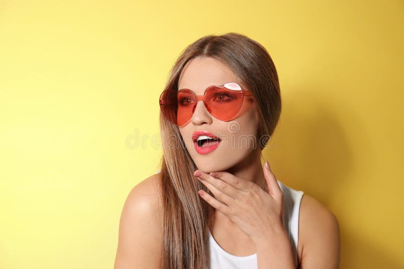 Young woman wearing stylish heart shaped sunglasses on background