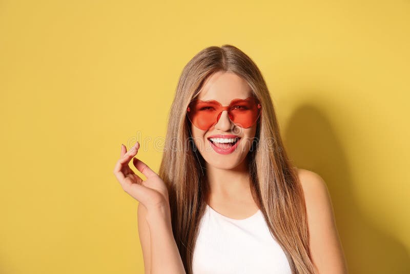 Young woman wearing stylish heart shaped sunglasses on yellow background