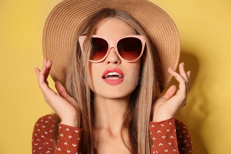 Young woman wearing stylish sunglasses and hat on background