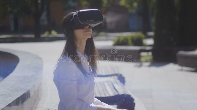 Close up young woman wearing vr glasses, headset, playing virtual games and watching videos outdoors in the beautiful