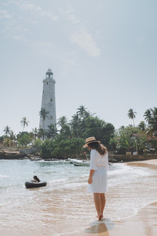 Young woman in white dress and hat walking along the beach against the lighthouse royalty free stock images Young woman in white dress and hat walking along the beach against the lighthouse royalty free stock images