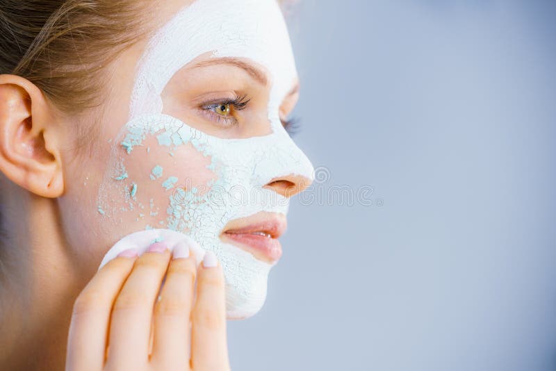 Young woman with white dried mud mask on face being removing cosmetic with cotton swab. Teen girl taking care of oily skin. Beauty treatment. Skincare. Young woman with white dried mud mask on face being removing cosmetic with cotton swab. Teen girl taking care of oily skin. Beauty treatment. Skincare