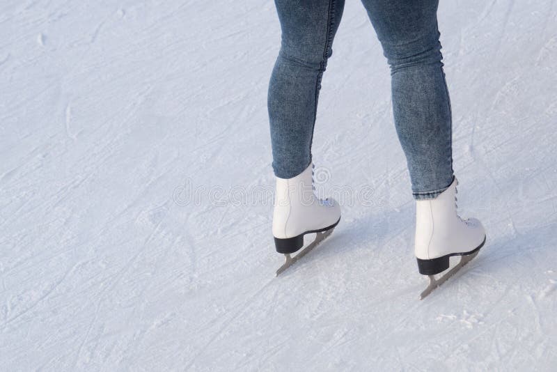 A young woman in white figure skates and blue jeans.