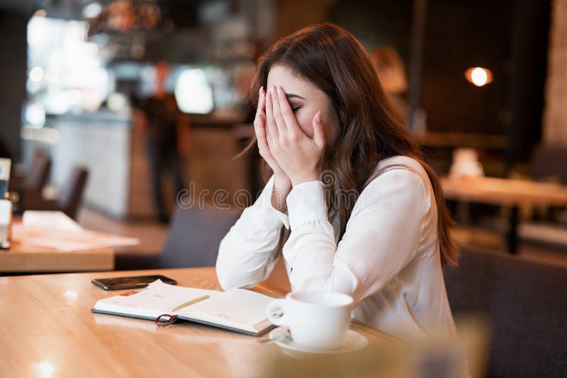 Young woman in white jacket working outside office during lunch break looking exhausted drinking hot coffee in the trendy cafe