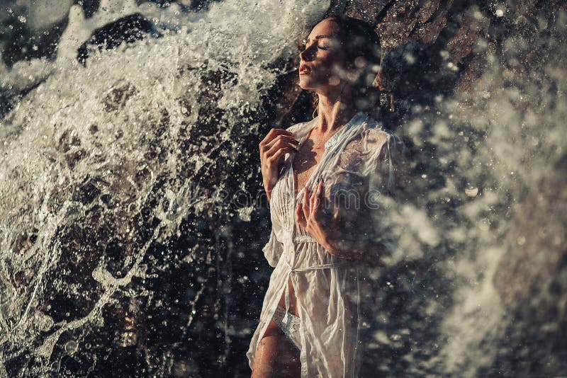 Young woman in white shirt and bikini stands in water flows near