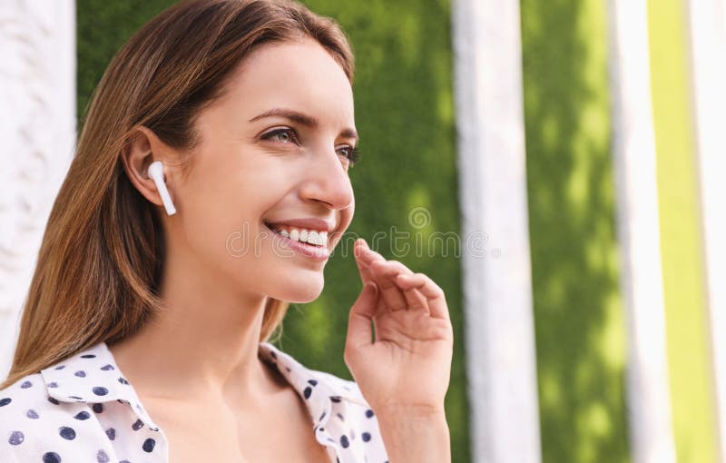 Young woman with wireless headphones listening to music near green grass wall