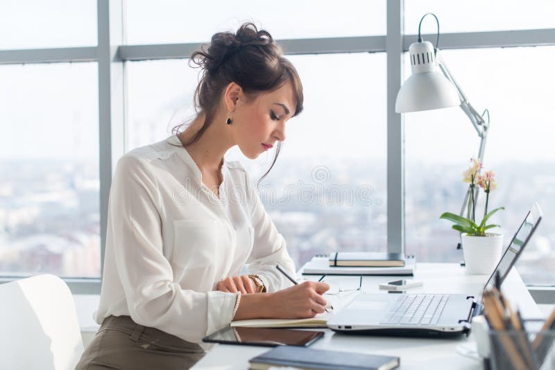 Young woman working as an office manager, planning work tasks, writing down her schedule to planner at the workplace. royalty free stock images Young woman working as an office manager, planning work tasks, writing down her schedule to planner at the workplace. royalty free stock images