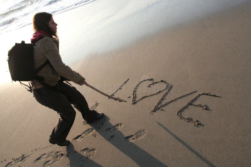 Young woman writing LOVE in the sand