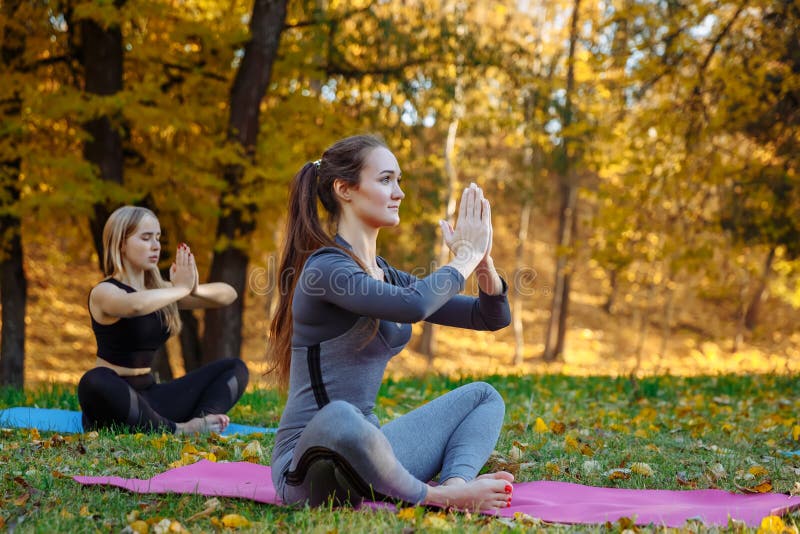 Group of Young women doing yoga exercises in the autumn city park. Health lifestyle concept.