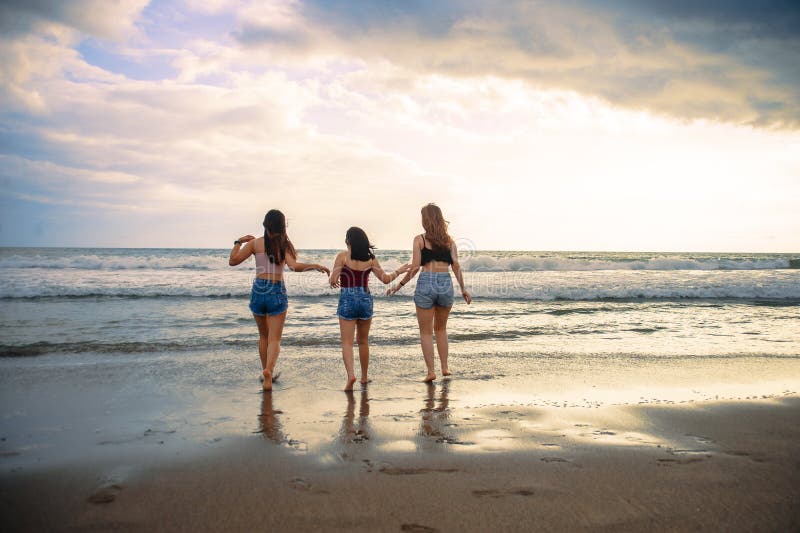 Young women friends or sisters playing together in the beach on sunset light having fun enjoying summer holidays trip in girlfrien