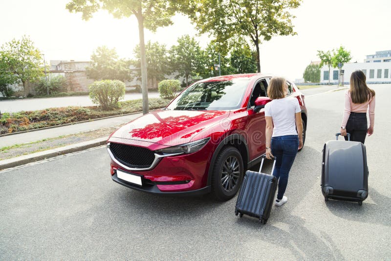 Young women going to travel by car and walking to it with two huge suitcases. Young women going to travel by car and walking to it with two huge suitcases