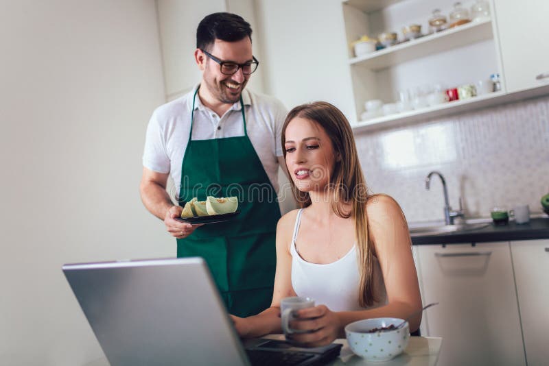 Woman working on laptop in kitchen as boyfriend prepares meal stock photos Woman working on laptop in kitchen as boyfriend prepares meal stock photos