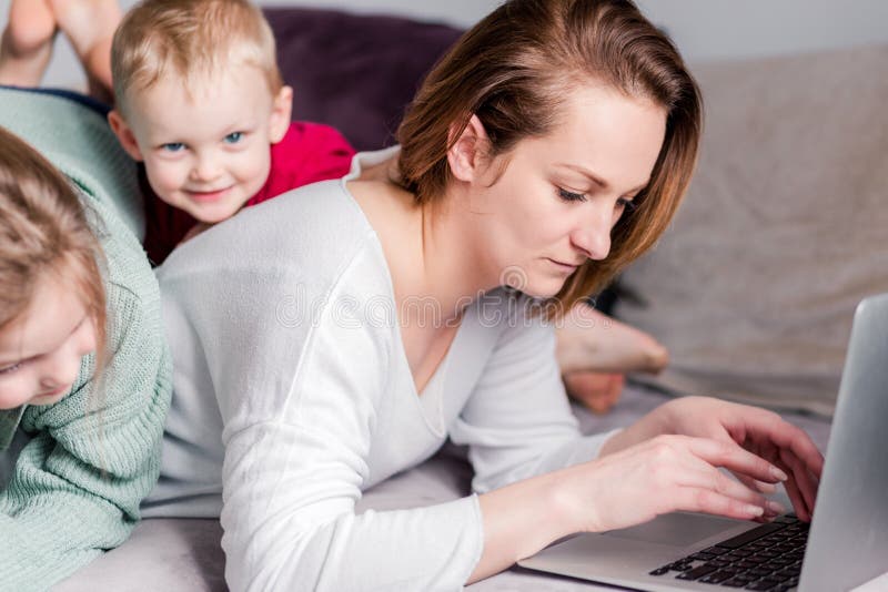 Young women works at home with laptop along with two children.Children want to communicate with mother, make noise and interfere royalty free stock photography Young women works at home with laptop along with two children.Children want to communicate with mother, make noise and interfere royalty free stock photography