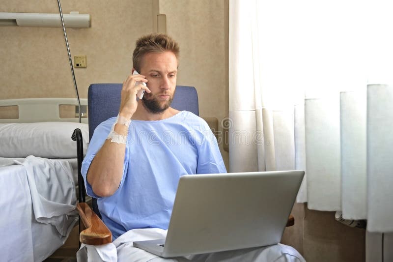 Young workaholic business man in hospital room sick and injured after accident working with mobile phone and computer laptop