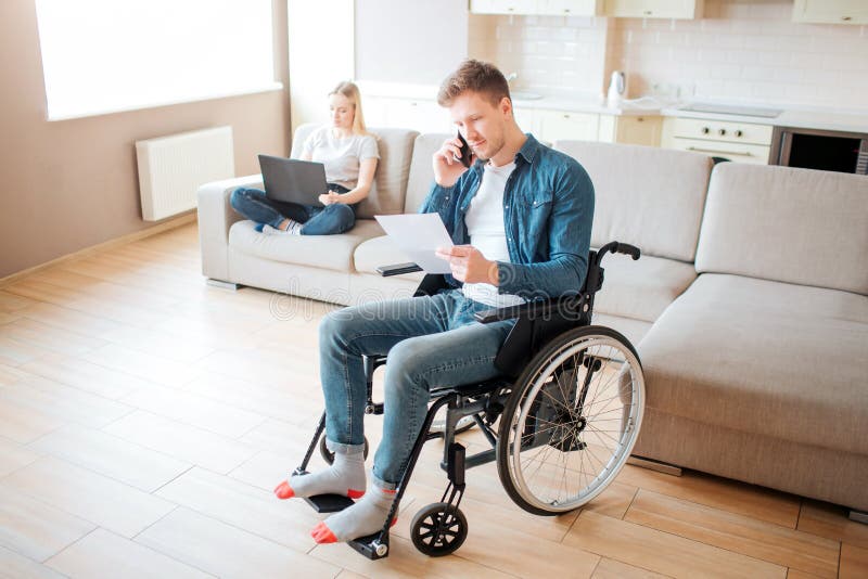 Young worker with disability in room. Holding piece of paper and talking on phone. Young woman sit behind on couch with stock images Young worker with disability in room. Holding piece of paper and talking on phone. Young woman sit behind on couch with stock images