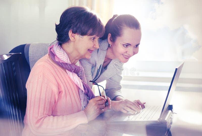 Younger woman helping an elderly person using laptop