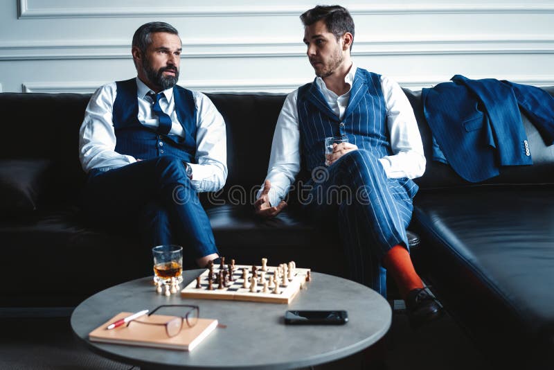 Focused man sipping alcoholic beverage while thinking about next chess move.  Stock Photo by DC_Studio