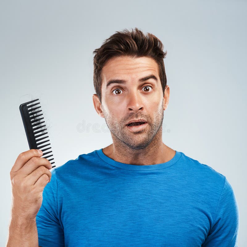 This is yours. Portrait of a young man with a confused facial expression holding a hair comb while standing against a royalty free stock photos