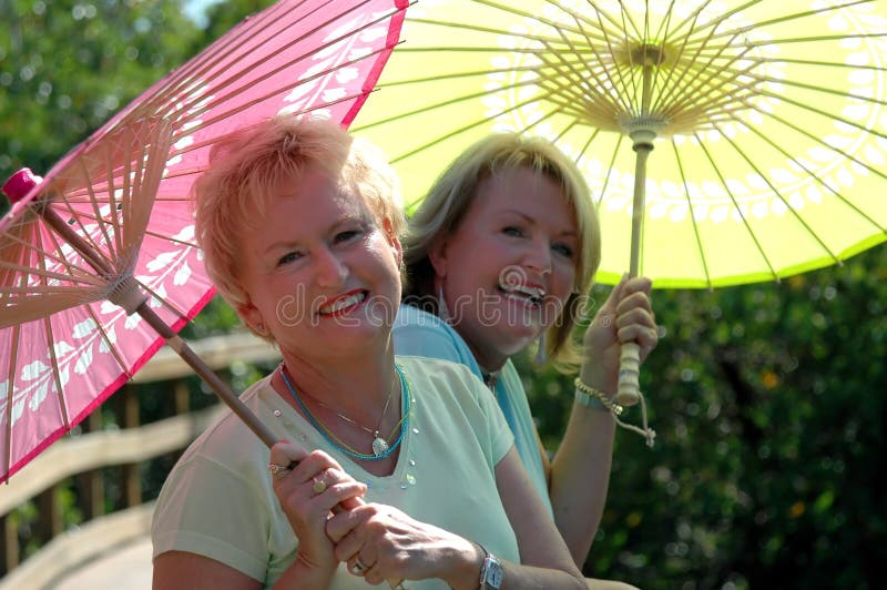 Dve zrelé ženy vonku na drevený chodník s farebnými slnečníkmi.