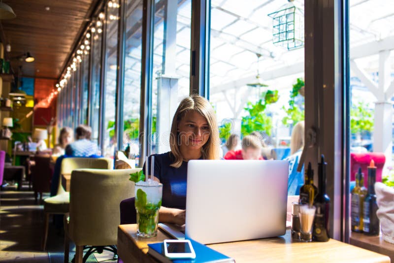 Yrkesmässig författare för kvinna som arbetar på netbook som sitter med drycken i coffee shop royaltyfri bild Yrkesmässig författare för kvinna som arbetar på netbook som sitter med drycken i coffee shop royaltyfri bild