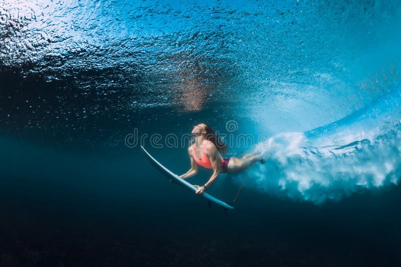Yrkesmässig surfarekvinna med surfingbrädadyken som är undervattens- med den under-stora havvågen