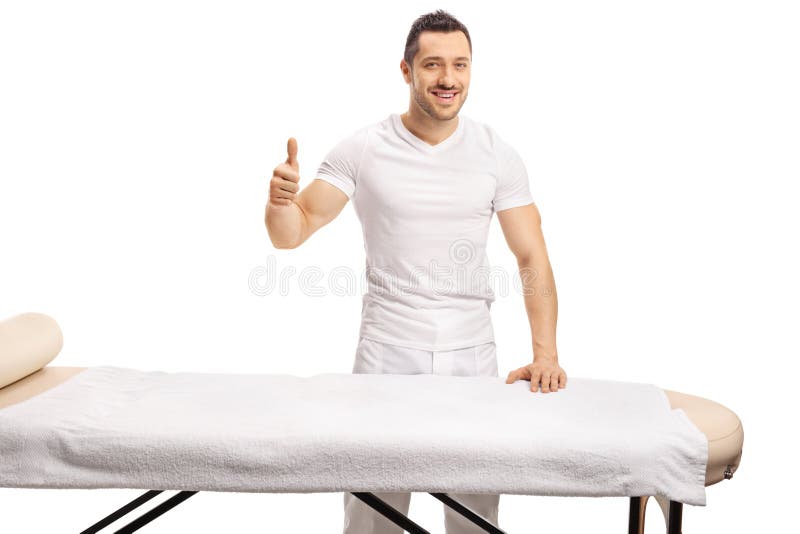 Professional masseur standing behind a massage bed and showing thumbs up isolated on white background. Professional masseur standing behind a massage bed and showing thumbs up isolated on white background