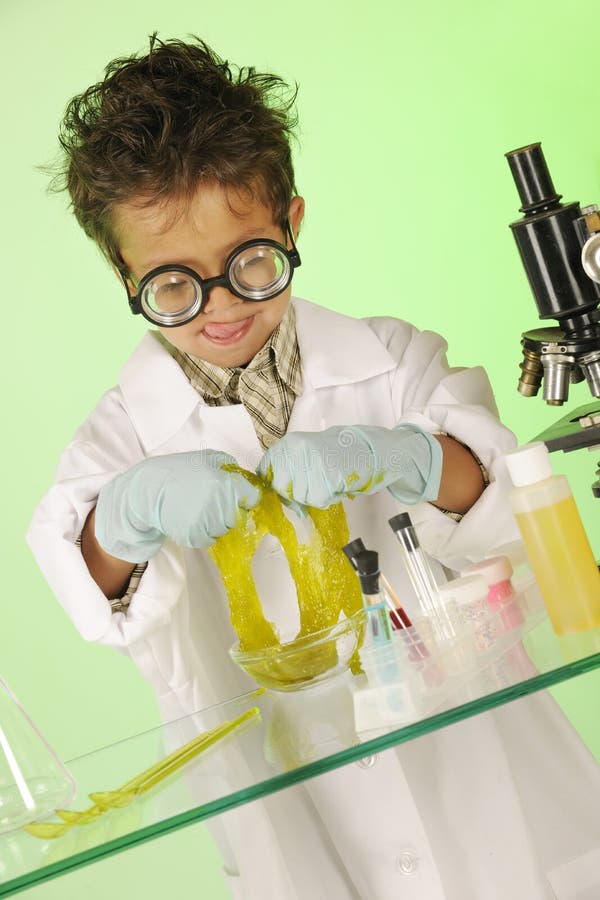 An adorable preschooler in coke bottle glasses and protective science wear, licking his lips while handling slime near test tubes, bottles and a microscope. An adorable preschooler in coke bottle glasses and protective science wear, licking his lips while handling slime near test tubes, bottles and a microscope.