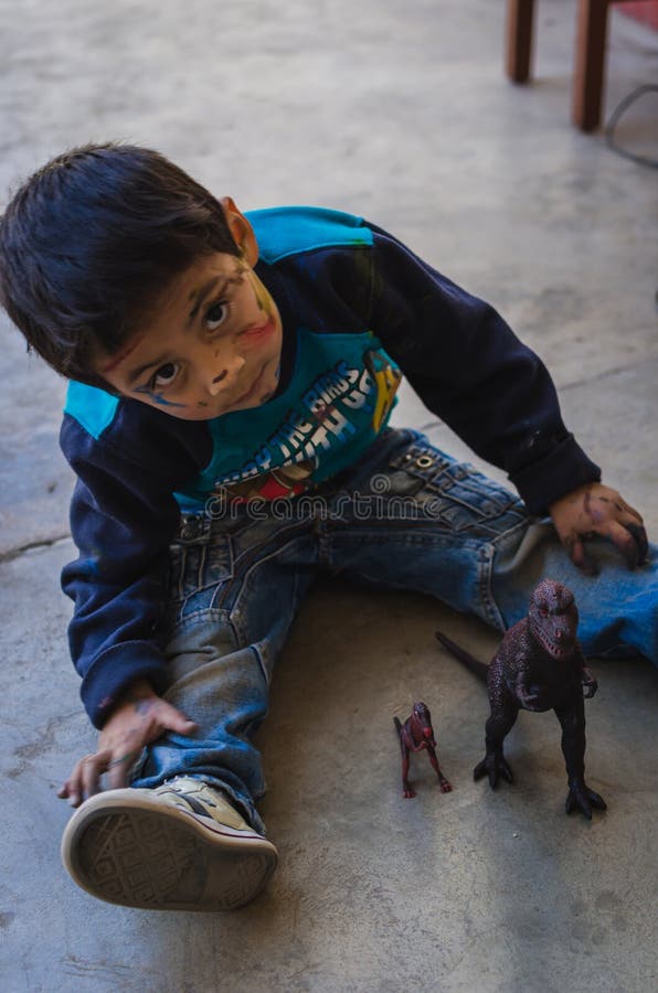 Yungay, Peru, August 4, 2014: Latino little boy with indigenous features with a dirty face of paint playing with t-rex toys