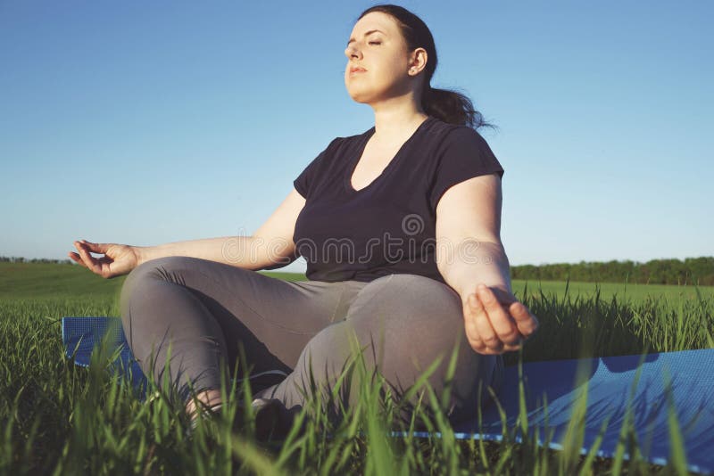 Z nadwagą kobieta medytuje przy joga matą outdoors obraz stock Z nadwagą kobieta medytuje przy joga matą outdoors obraz stock