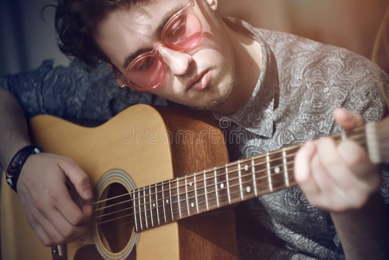 Z włosami facet z różowymi szkłami bawić się drewnianą gitary akustycznej melodię obrazy royalty free Z włosami facet z różowymi szkłami bawić się drewnianą gitary akustycznej melodię obrazy royalty free