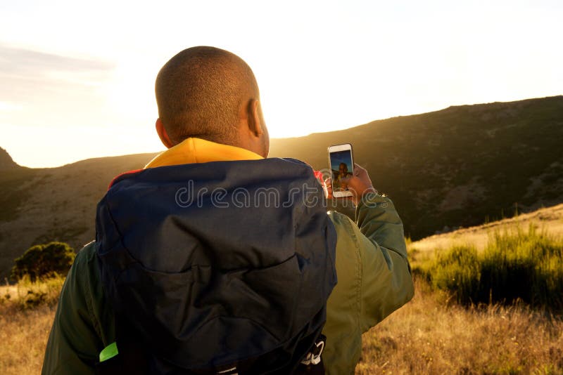 Za amerykanin afrykańskiego pochodzenia mężczyzną wycieczkuje z telefonem komórkowym bierze selfie w górach fotografia stock Za amerykanin afrykańskiego pochodzenia mężczyzną wycieczkuje z telefonem komórkowym bierze selfie w górach fotografia stock