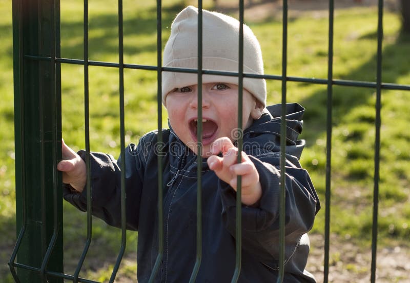 A toddler with a cheerful expression opening an iron gate; grass in the background. A toddler with a cheerful expression opening an iron gate; grass in the background.