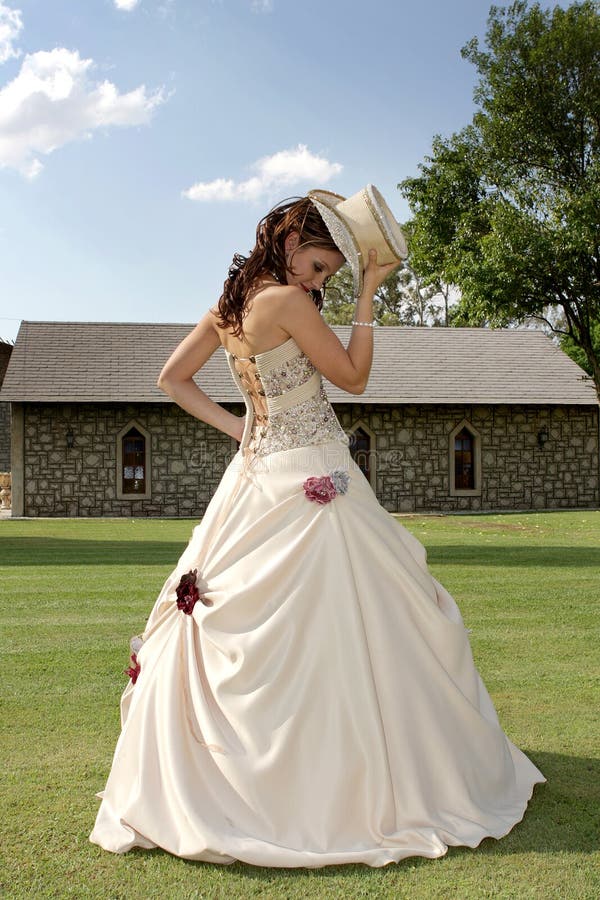 A bride standing on grass holding a hat. A bride standing on grass holding a hat