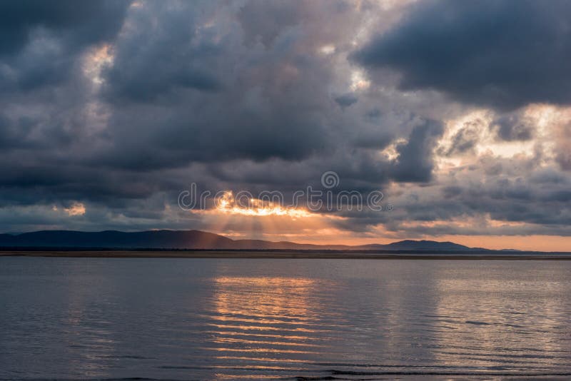 Sun rays peek through the dark and grey clouds during sunset as it paints part of the waters with a beautiful orange colour. Sun rays peek through the dark and grey clouds during sunset as it paints part of the waters with a beautiful orange colour.