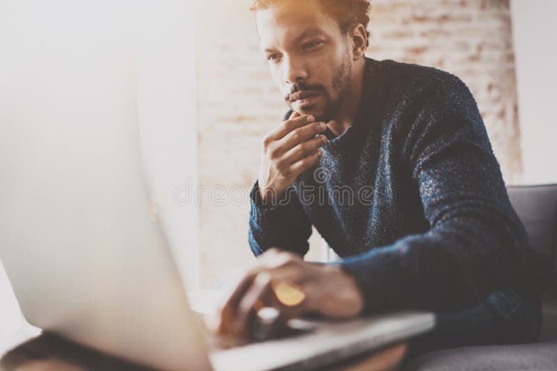 Zadumany młody Afrykański biznesmen używa laptop przy jego nowożytnym coworking miejscem podczas gdy siedzący na kanapie Pojęcie zdjęcie royalty free Zadumany młody Afrykański biznesmen używa laptop przy jego nowożytnym coworking miejscem podczas gdy siedzący na kanapie Pojęcie zdjęcie royalty free