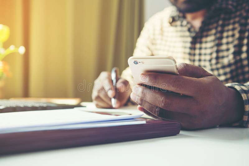 Casual business man using mobile smart phone working, taking note, schedule on paper notebook, reading e book application. E. Casual business man using mobile smart phone working, taking note, schedule on paper notebook, reading e book application. E