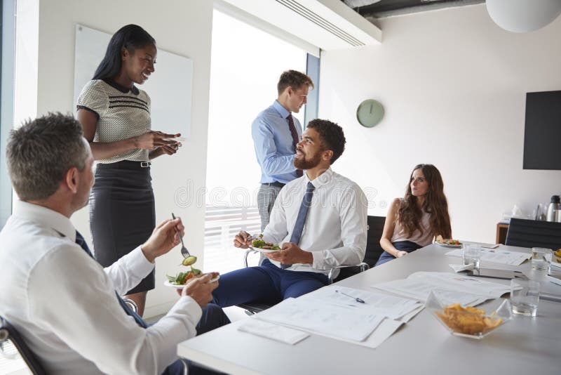 Zakenlieden en Onderneemsters die in Moderne Bestuurskamer bij Werkende Lunch samenkomen royalty-vrije stock foto Zakenlieden en Onderneemsters die in Moderne Bestuurskamer bij Werkende Lunch samenkomen royalty-vrije stock foto