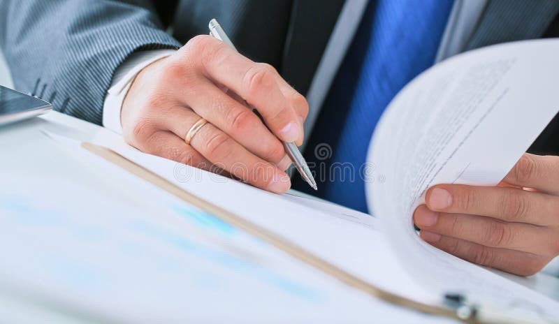 Cropped image of businessman in dark suit sitting at office desk signing a contract with shallow focus on signature. Cropped image of businessman in dark suit sitting at office desk signing a contract with shallow focus on signature.