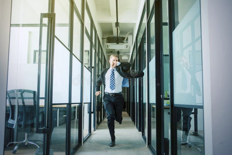 Handsome Caucasian businessman checking his watch while rushing and running on the office hallway. Handsome Caucasian businessman checking his watch while rushing and running on the office hallway