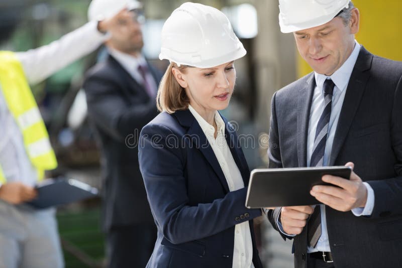 Zakenman en onderneemster die digitale tablet met collega's op achtergrond gebruiken bij de industrie royalty-vrije stock afbeeldingen Zakenman en onderneemster die digitale tablet met collega's op achtergrond gebruiken bij de industrie royalty-vrije stock afbeeldingen