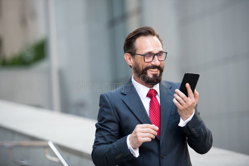 Zakenman in glazen die slimme telefoon op bureaugang met behulp van met stad de bouwachtergrond Concept bedrijfsmensen stock foto Zakenman in glazen die slimme telefoon op bureaugang met behulp van met stad de bouwachtergrond Concept bedrijfsmensen stock foto