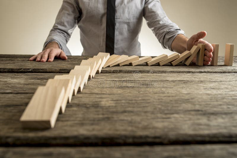 Businessman hand stopping domino effect. Rough wooden table with copy space. Businessman hand stopping domino effect. Rough wooden table with copy space.